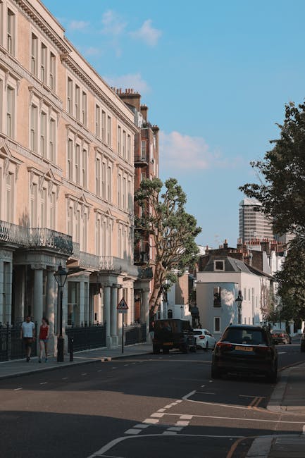 A street scene in Maida Vale showing a row of elegant, white Victorian-style terraced houses with ornate architectural details, large sash windows, and decorative balconies. Several leafless trees lin