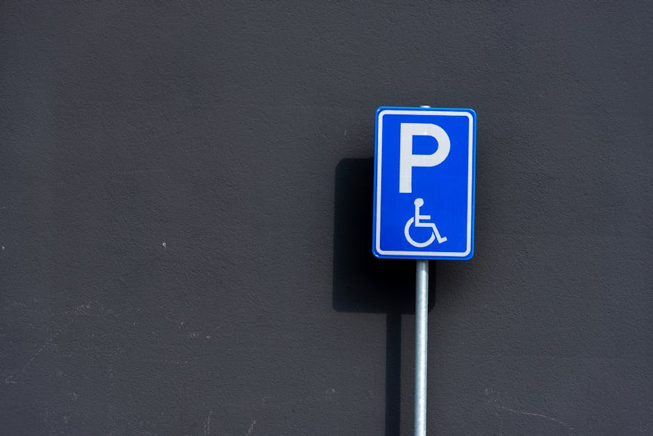 A close-up of a green parking restriction sign mounted on a metal post in an outdoor urban environment, indicating a two-hour parking limit from 8 a.m. to 8 p.m., Monday to Saturday, with no parking on Sundays. The sign is in front of a background of a partly cloudy blue sky and blurred green trees. The sign's metal post shows some signs of rust, and the sign itself has minor scratches and a small section of peeling paint. This image relates to parking regulations that may affect home relocation or furniture transport processes in Maida Vale, where Removal Van Maida Vale provides professional removals services and assistance with parking permits to facilitate efficient moving and packing operations.