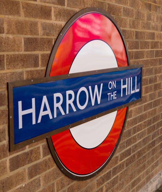 Indoor view of Baker Street underground station platform in Maida Vale, featuring two large illuminated station maps in protective frames on brick walls, with wooden benches below each map. The station name 'BAKER STREET' is displayed on signs above the maps and on a circular underground logo mounted between them. A blurred figure of a person is walking past on the right side of the image. The environment includes brick archways, a tiled ceiling, and signage related to London Underground clearly visible. The scene captures the typical setting for home relocation and furniture transport logistics, with the station environment providing context for the transportation of household items and packing materials used during removals, as managed by Removal Van Maida Vale.